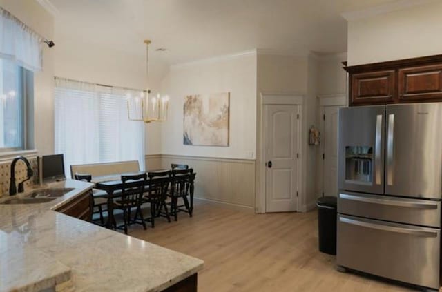 kitchen with a notable chandelier, a sink, light wood finished floors, a wainscoted wall, and stainless steel refrigerator with ice dispenser