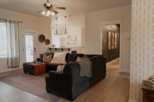 living area featuring light wood-style floors, a ceiling fan, baseboards, and crown molding