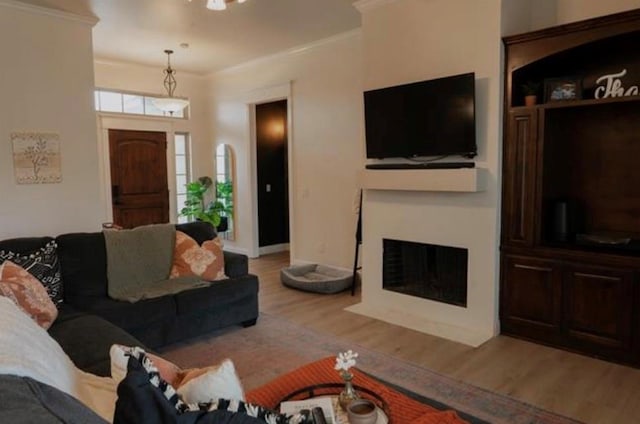 living room featuring light wood-style floors, baseboards, ornamental molding, and a fireplace with flush hearth