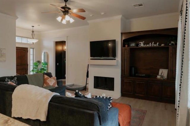living room featuring a fireplace, a ceiling fan, wood finished floors, visible vents, and ornamental molding