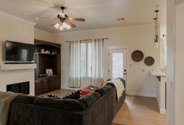 living room with crown molding, baseboards, ceiling fan, and light wood finished floors