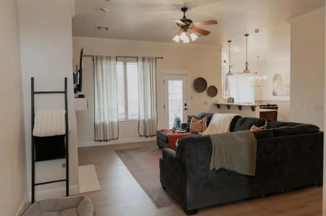living area featuring light wood-type flooring, ornamental molding, baseboards, and ceiling fan