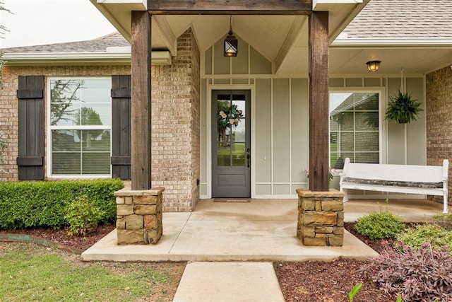 view of exterior entry featuring brick siding, a shingled roof, board and batten siding, and a porch