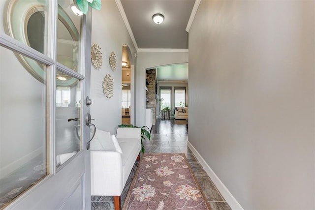 hallway with arched walkways, ornamental molding, baseboards, and stone tile flooring