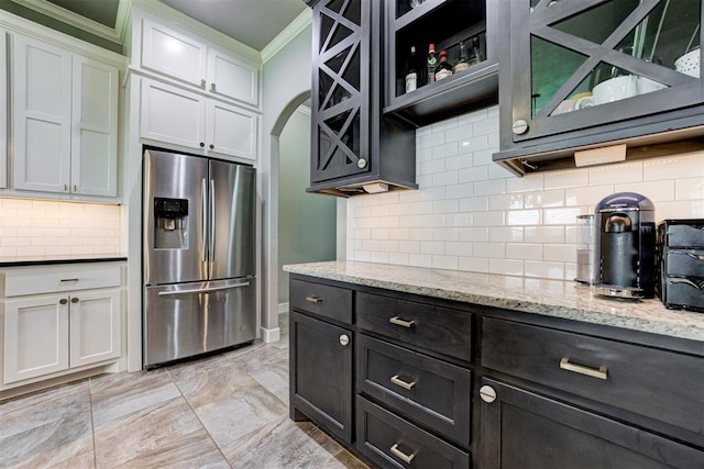 kitchen with stainless steel refrigerator with ice dispenser, tasteful backsplash, light stone countertops, ornamental molding, and white cabinetry