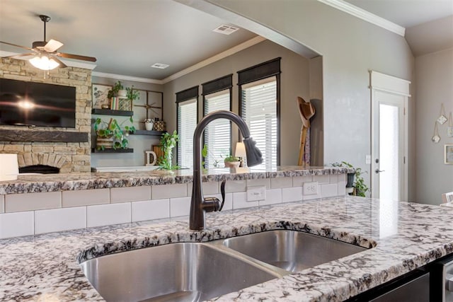 kitchen with light stone countertops, a sink, a ceiling fan, visible vents, and ornamental molding
