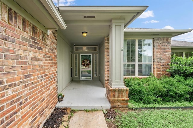 property entrance featuring visible vents, a shingled roof, and brick siding