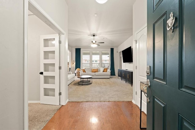 entrance foyer featuring light wood-style floors, baseboards, a ceiling fan, and light colored carpet