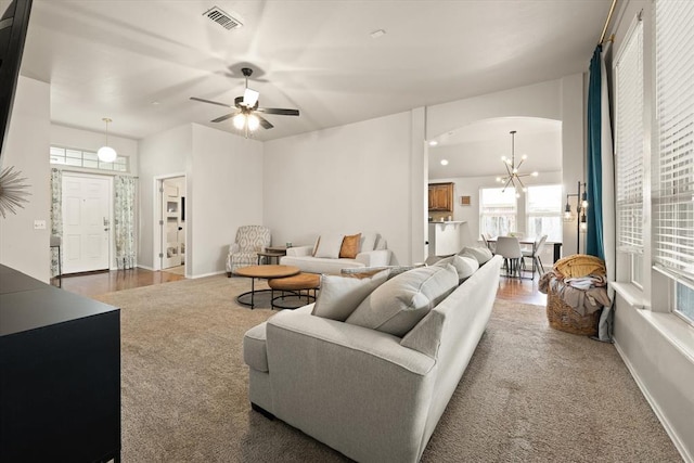 carpeted living room with visible vents, arched walkways, baseboards, and ceiling fan with notable chandelier