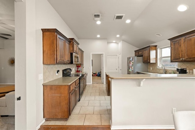kitchen with appliances with stainless steel finishes, tasteful backsplash, light countertops, a peninsula, and lofted ceiling