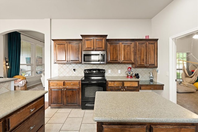 kitchen featuring plenty of natural light, tasteful backsplash, stainless steel microwave, and black range with electric stovetop