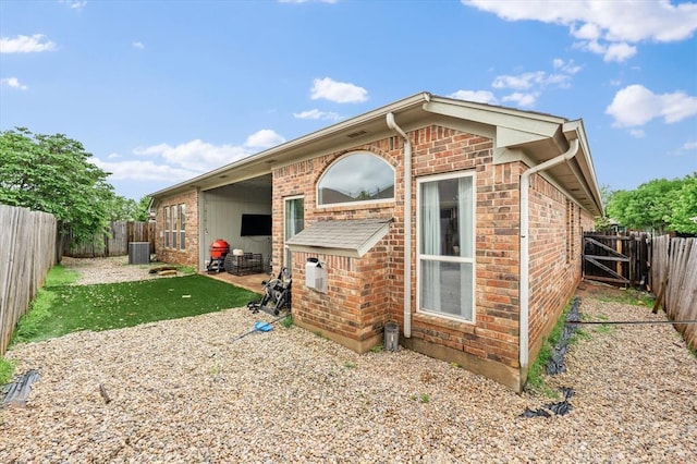rear view of property with brick siding, cooling unit, a fenced backyard, and a patio area