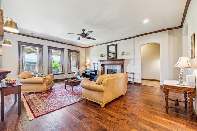 living area with a ceiling fan, wood-type flooring, crown molding, arched walkways, and a tile fireplace