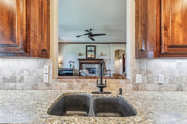 kitchen with light stone countertops, decorative backsplash, a ceiling fan, and a sink