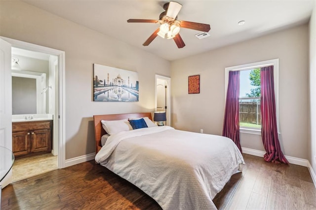 bedroom with connected bathroom, wood finished floors, visible vents, baseboards, and ceiling fan