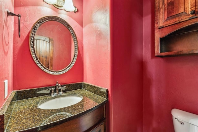 bathroom with toilet, vanity, and a textured wall
