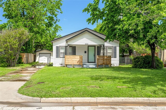 bungalow-style home with covered porch, fence, an outbuilding, and a front yard