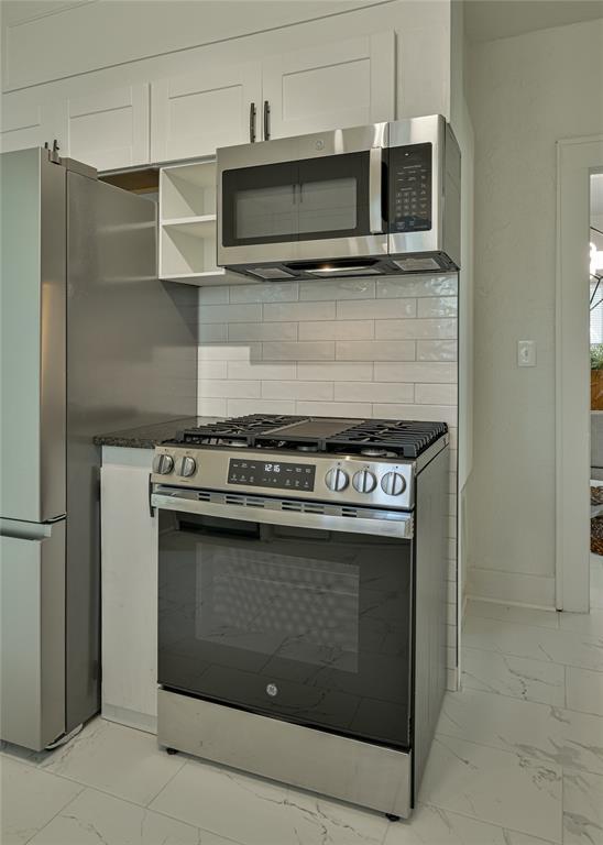 kitchen with tasteful backsplash, stainless steel appliances, white cabinetry, and marble finish floor