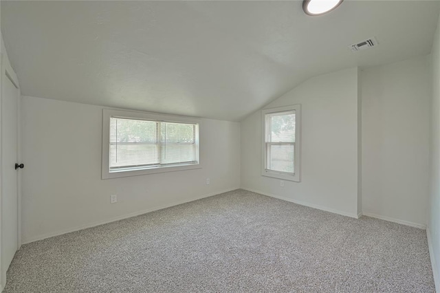 empty room with carpet flooring, baseboards, visible vents, and vaulted ceiling