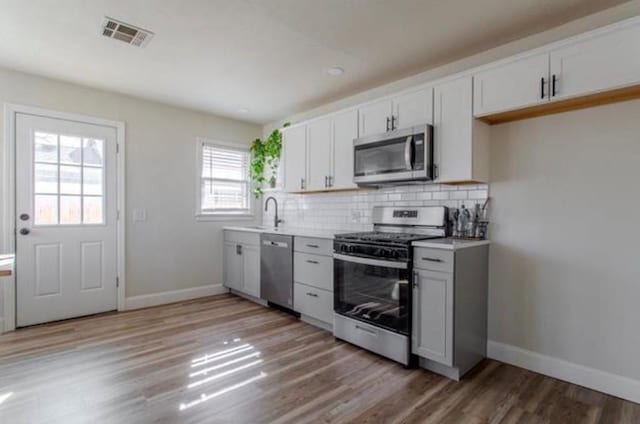 kitchen featuring stainless steel appliances, baseboards, visible vents, and light wood-style floors