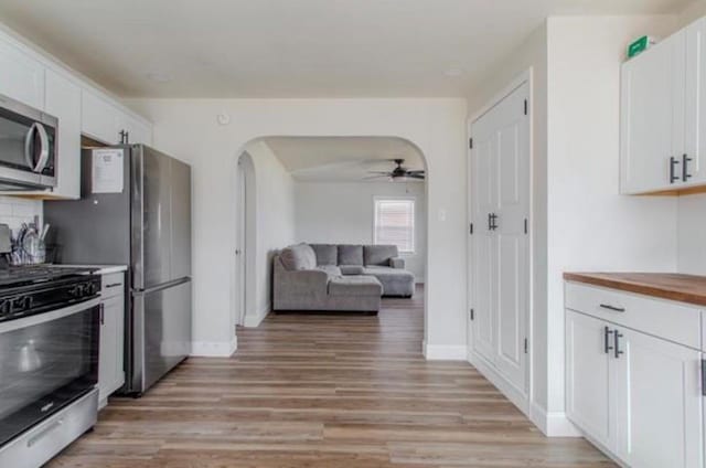 kitchen with arched walkways, white cabinets, stainless steel appliances, and light wood-style flooring