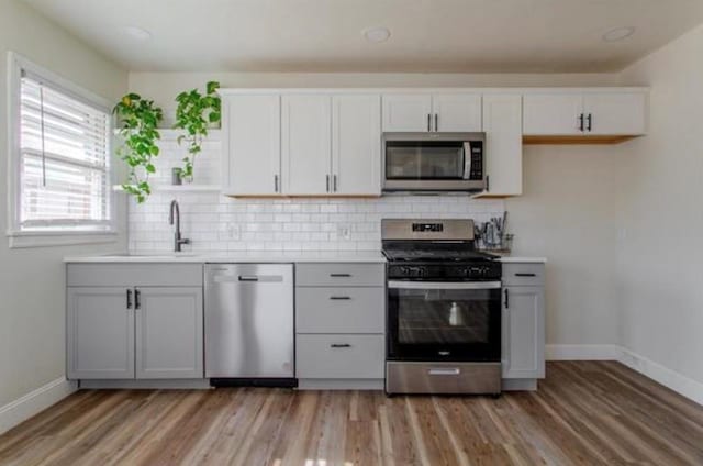 kitchen featuring appliances with stainless steel finishes, tasteful backsplash, light wood-type flooring, a sink, and baseboards