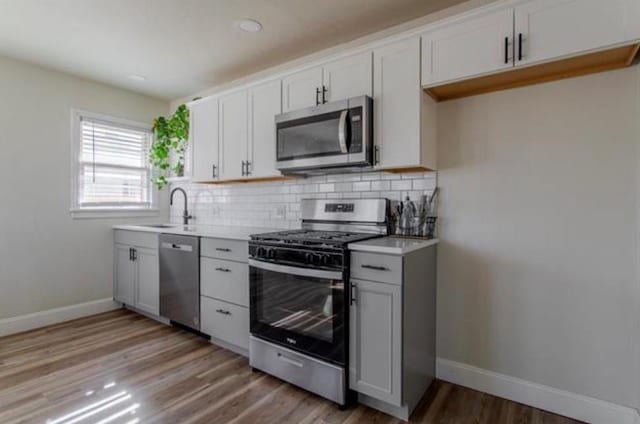 kitchen featuring a sink, light wood finished floors, stainless steel appliances, baseboards, and decorative backsplash