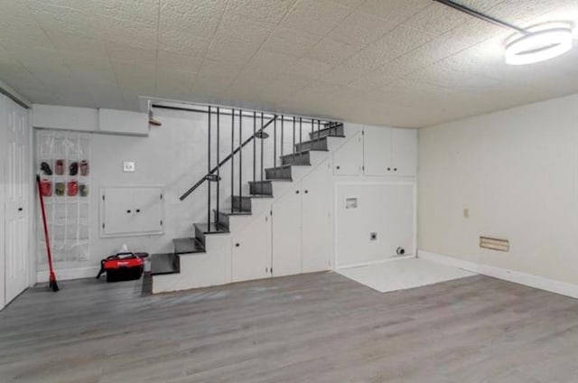 finished below grade area with baseboards, wood finished floors, and stairway