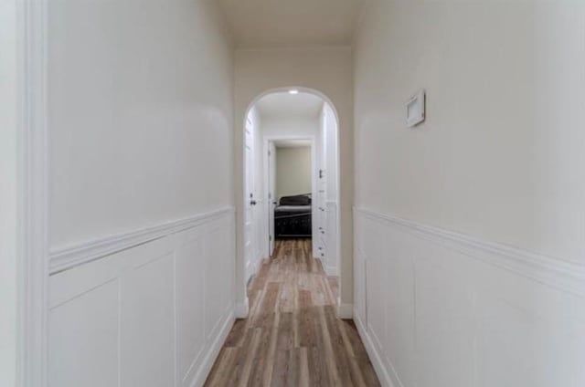 hallway featuring a wainscoted wall, a decorative wall, light wood-type flooring, and arched walkways