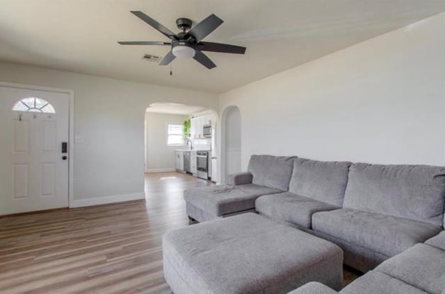 living room with a ceiling fan, visible vents, arched walkways, light wood-type flooring, and baseboards