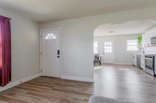 foyer with arched walkways, baseboards, and light wood-type flooring