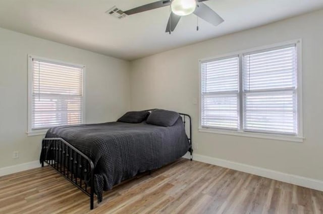 bedroom with baseboards, multiple windows, wood finished floors, and visible vents