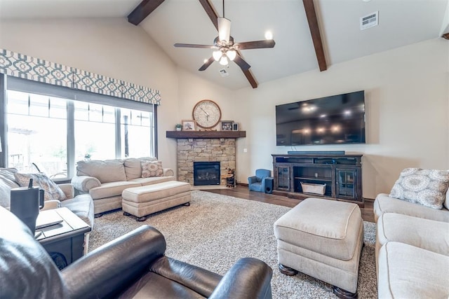 living room featuring a ceiling fan, a stone fireplace, visible vents, wood finished floors, and beam ceiling