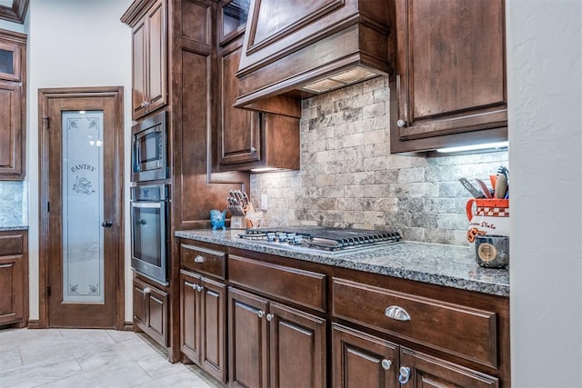 kitchen featuring stone countertops, backsplash, dark brown cabinets, and stainless steel appliances