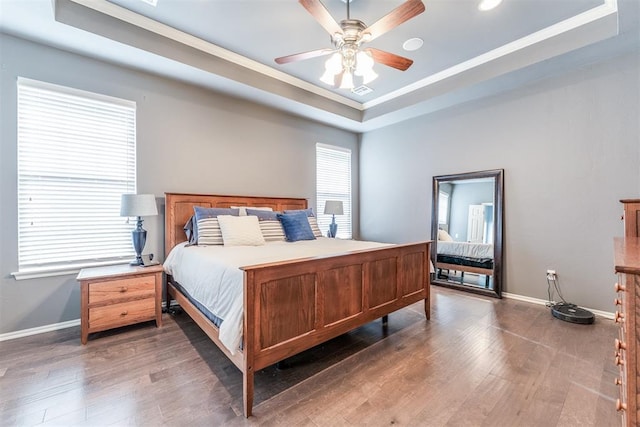 bedroom featuring crown molding, wood finished floors, a raised ceiling, baseboards, and recessed lighting