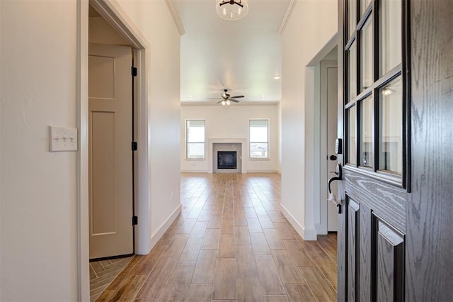 entryway featuring a ceiling fan, baseboards, a glass covered fireplace, and light wood-style floors
