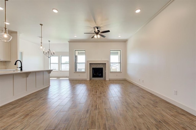 unfurnished living room featuring ornamental molding, baseboards, light wood-type flooring, recessed lighting, and ceiling fan with notable chandelier