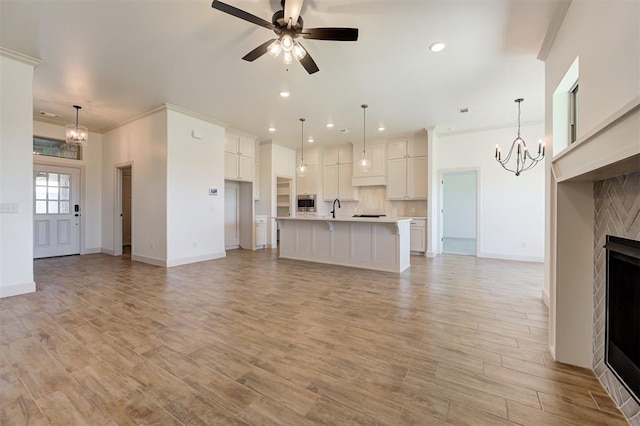 unfurnished living room with baseboards, recessed lighting, crown molding, and ceiling fan with notable chandelier