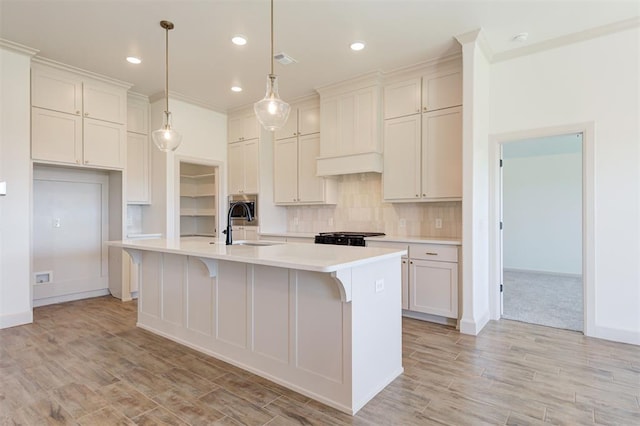 kitchen with a sink, light wood finished floors, light countertops, a kitchen island with sink, and wall chimney exhaust hood