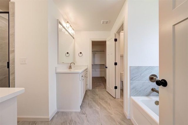 bathroom with a walk in closet, vanity, baseboards, toilet, and a tub to relax in