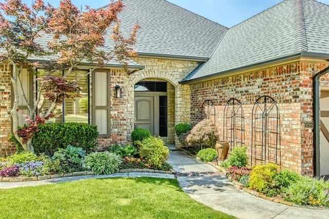 property entrance with a yard, brick siding, a shingled roof, and stone siding