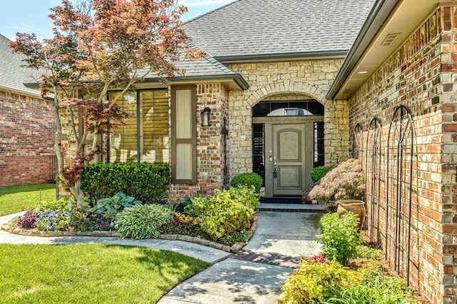 view of exterior entry with brick siding and a shingled roof