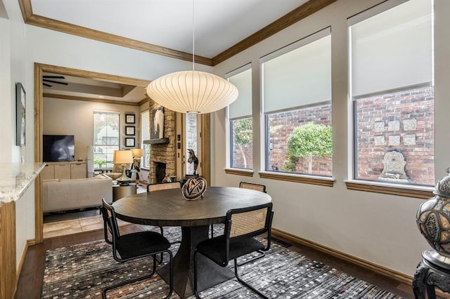 dining area with dark wood-type flooring, ornamental molding, baseboards, and a fireplace