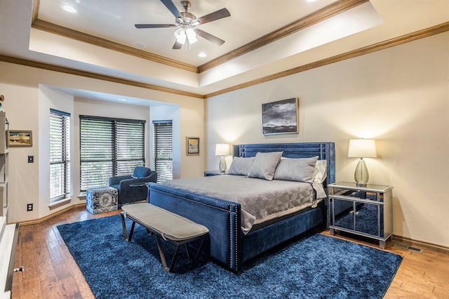 bedroom with baseboards, a tray ceiling, visible vents, ornamental molding, and hardwood / wood-style flooring