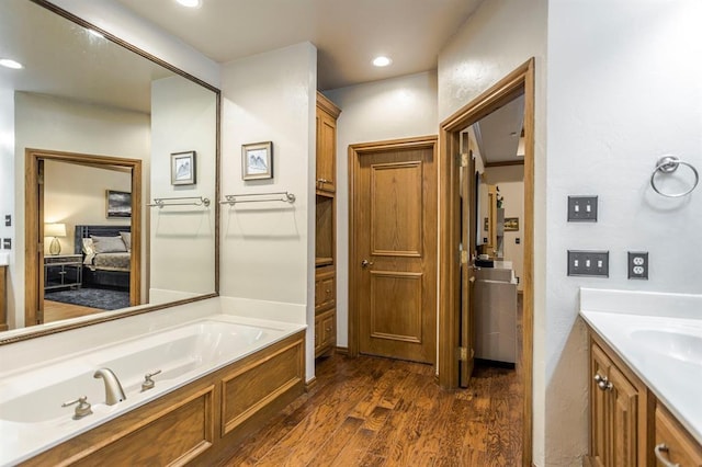 bathroom with recessed lighting, wood finished floors, a bath, and vanity