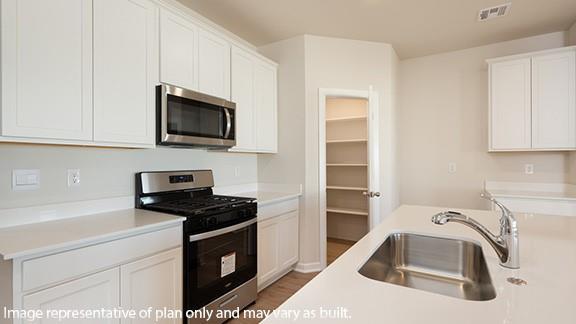 kitchen with a sink, appliances with stainless steel finishes, white cabinetry, and visible vents