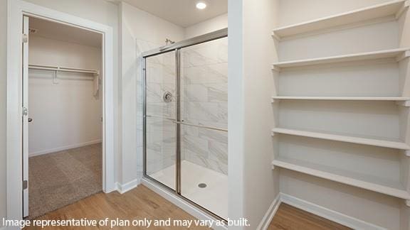 full bath featuring a walk in closet, baseboards, a shower stall, and wood finished floors