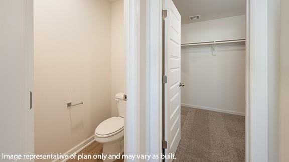 bathroom with toilet, baseboards, visible vents, and a walk in closet