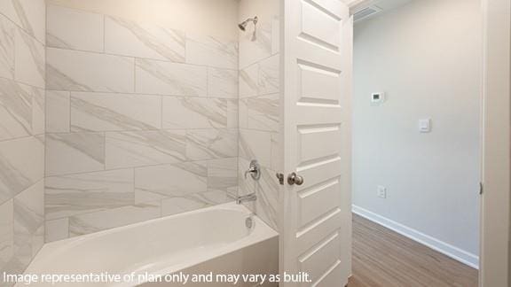 bathroom with baseboards, wood finished floors, and shower / washtub combination