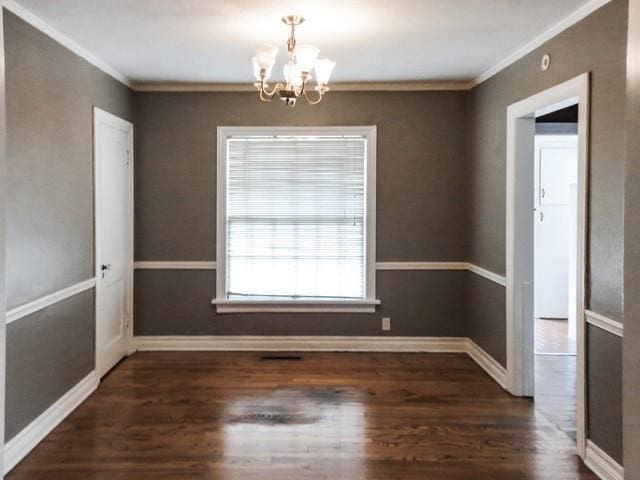unfurnished room with an inviting chandelier, baseboards, crown molding, and wood finished floors